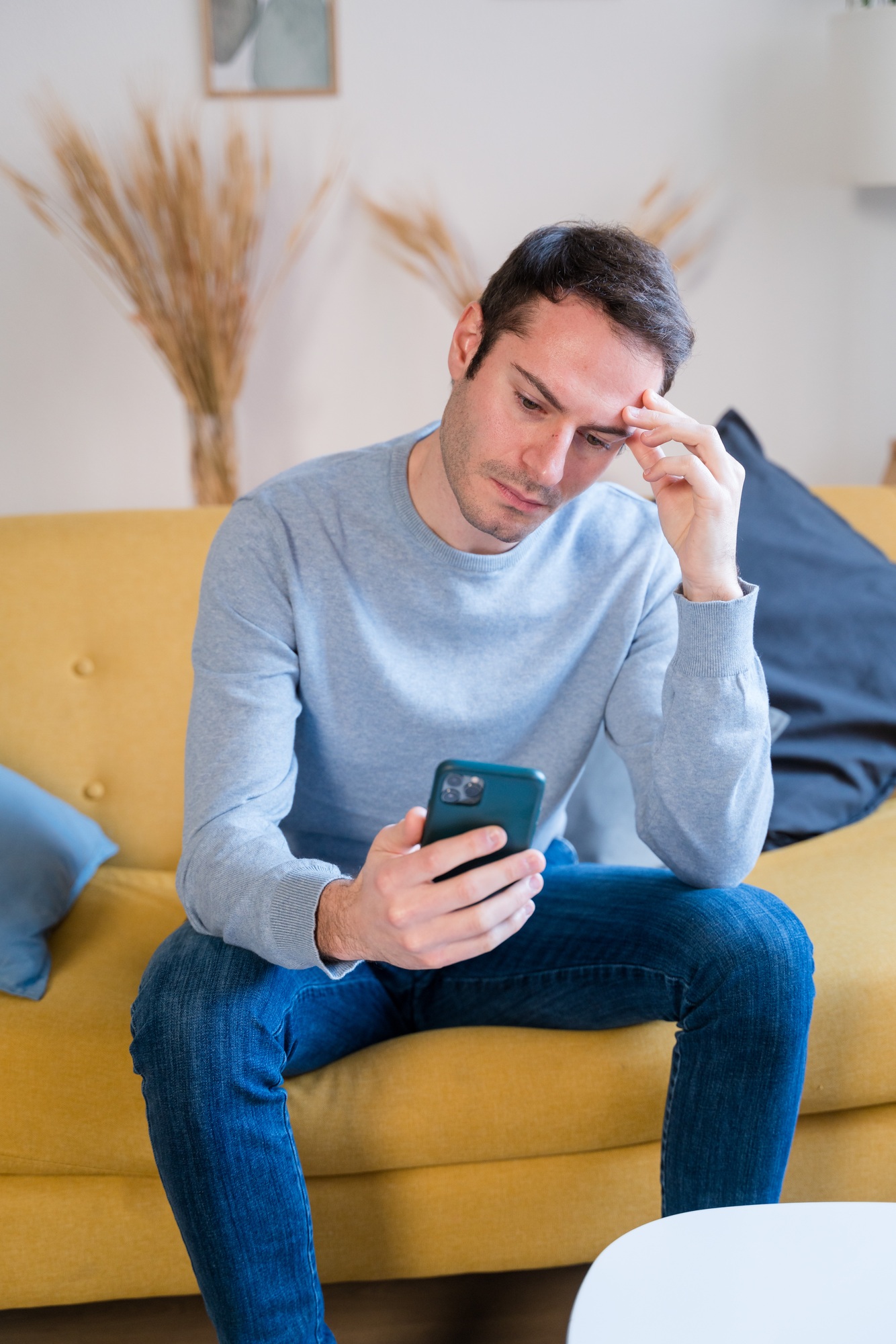 Stressed man using smartphone on sofa at home